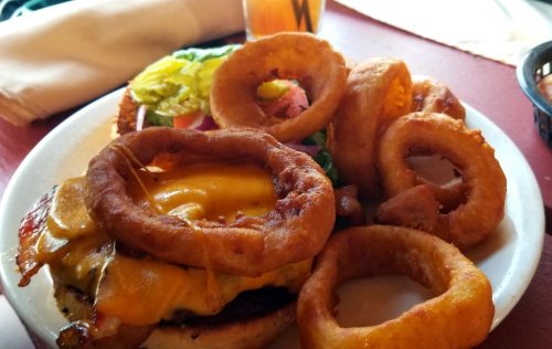 A plate featuring a cheeseburger topped with onion rings, lettuce, and tomato, accompanied by extra onion rings.