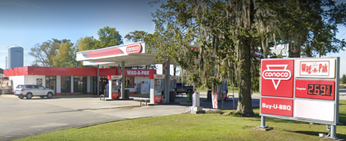 A Conoco gas station with a convenience store and a BBQ sign, surrounded by trees and grass.