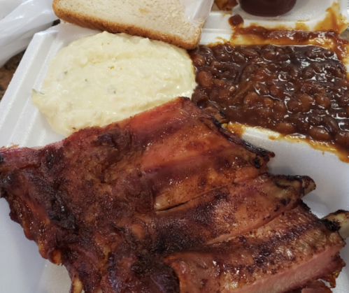 A plate featuring BBQ ribs, baked beans, creamy coleslaw, and a slice of bread.