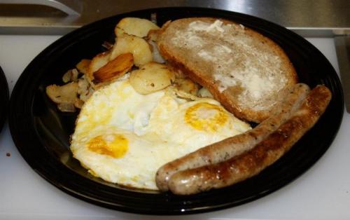 A black plate with two fried eggs, roasted potatoes, a slice of buttered toast, and two sausage links.
