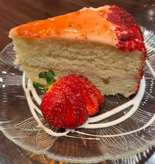 A slice of cake topped with strawberry glaze, served with a fresh strawberry on a glass plate.