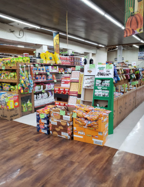 A colorful grocery store aisle filled with snacks, drinks, and various products on wooden shelves and displays.
