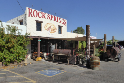 Exterior of a building labeled "Rock Springs," featuring rustic decor and outdoor seating in a sunny setting.