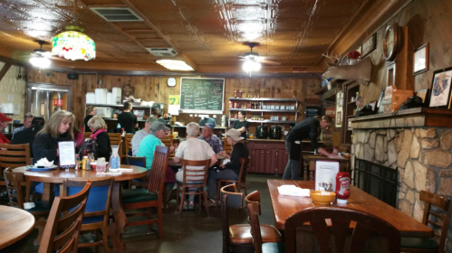 A cozy restaurant interior with wooden decor, diners at tables, and staff serving food near a stone fireplace.