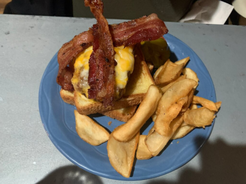 A plate with a bacon cheeseburger on toasted bread, accompanied by crispy potato wedges.