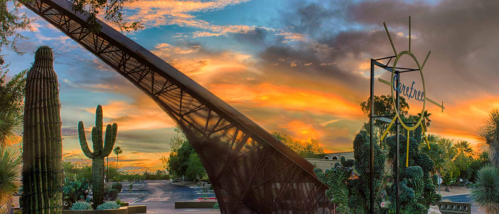 A sunset view featuring a large metal structure, cacti, and a sign, with vibrant orange and purple skies.