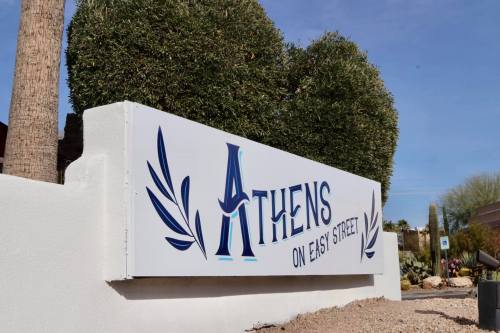 Sign for "Athens on East Street" with decorative elements, surrounded by greenery and desert landscaping.