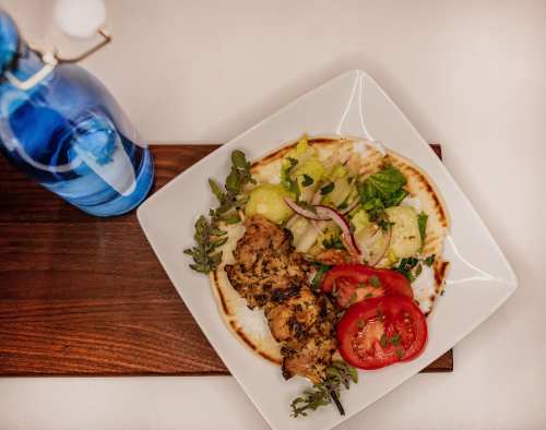 A plate of grilled chicken with fresh vegetables, served with a side of mashed potatoes and a bottle of water.