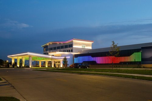 A modern building with colorful lighting at dusk, featuring a welcoming entrance and landscaped surroundings.