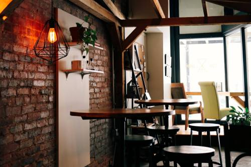 Cozy café interior with brick walls, wooden tables, and a warm light fixture, featuring plants and seating areas.