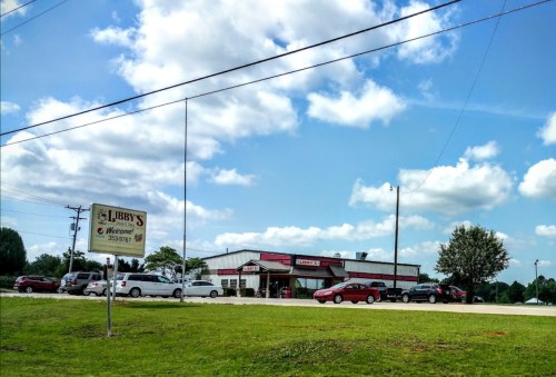 A restaurant named Libby's with a sign out front, surrounded by cars and green grass under a blue sky with clouds.