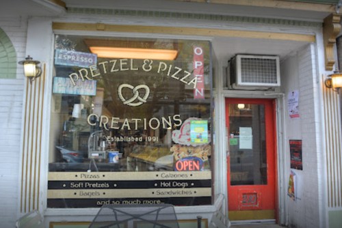 Exterior of a shop named "Pretzel & Pizza Creations," featuring a menu of pretzels, pizzas, and sandwiches.
