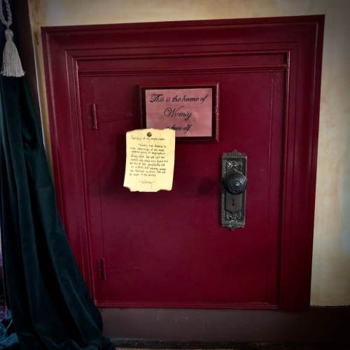 A red door with a sign reading "This is the home of Wendy" and a note attached, set against a dark curtain.