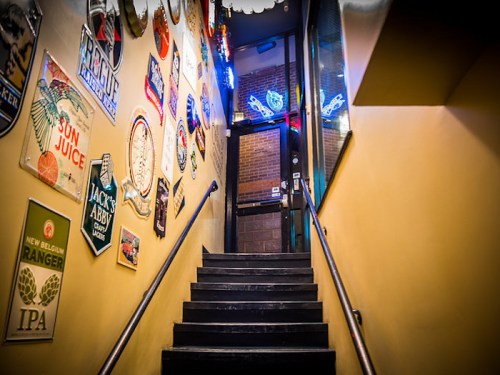 Staircase leading up to a door, lined with colorful vintage signs and illuminated by neon lights.