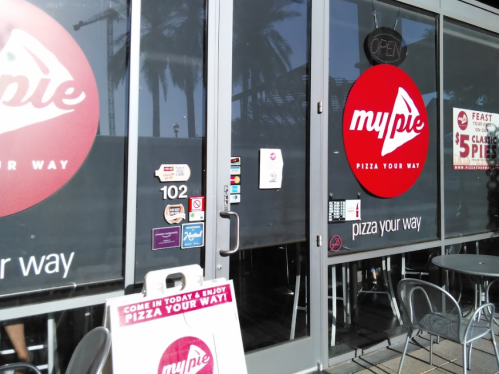 Exterior of My Pie restaurant with a red logo, open sign, and outdoor seating area.