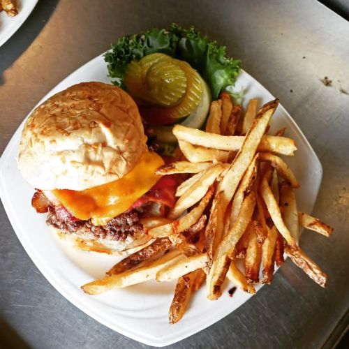 A juicy cheeseburger with bacon, lettuce, pickles, and a side of crispy fries on a white plate.
