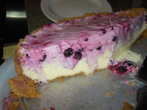 A slice of pink berry cheesecake with a graham cracker crust, revealing layers of creamy filling and berries.
