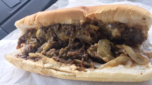 A close-up of a loaded sandwich filled with beef, melted cheese, and sautéed onions on a soft hoagie roll.