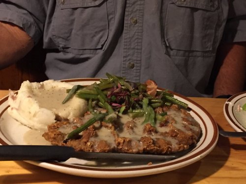 A plate of chicken-fried steak with gravy, green beans, and mashed potatoes on a wooden table.