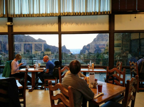 A cozy restaurant with wooden tables, featuring large windows showcasing a mountain view at sunset.