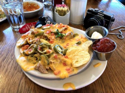 A plate of nachos topped with cheese, jalapeños, tomatoes, and served with salsa and sour cream on the side.