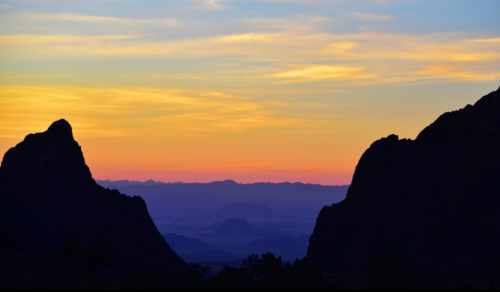 Silhouetted mountains against a colorful sunset sky with soft clouds and distant hills.