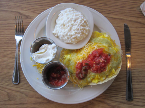 A plate with a cheesy egg dish, salsa, and a side of cottage cheese, served with forks and knives.