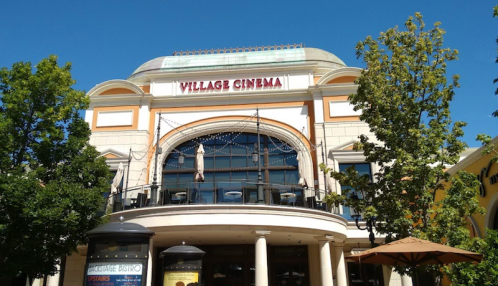 Exterior view of Village Cinema, featuring a large entrance and outdoor seating under a clear blue sky.