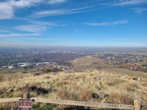 A panoramic view of a valley and cityscape from a hilltop, with blue skies and distant mountains in the background.
