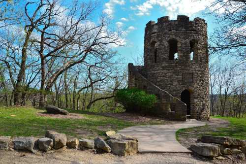 A stone tower with arched windows surrounded by trees and a winding path on a sunny day.