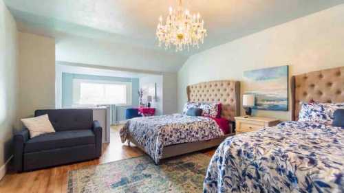 A spacious bedroom with two beds, a chandelier, and a cozy seating area, featuring floral decor and warm lighting.