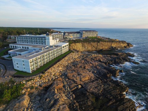 A coastal hotel perched on rocky cliffs, overlooking the ocean under a clear sky.