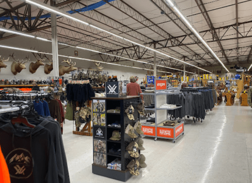A spacious retail store aisle filled with outdoor gear, clothing, and mounted animal heads on the walls.