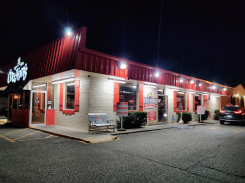 A brightly lit fast-food restaurant at night with red accents and a sign reading "CooCoo's." Parking area visible.