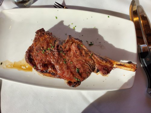 A perfectly cooked, juicy tomahawk steak garnished with herbs on a white plate, with cutlery beside it.