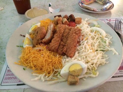 A large salad topped with crispy chicken strips, shredded cheese, croutons, sliced eggs, and mixed greens.
