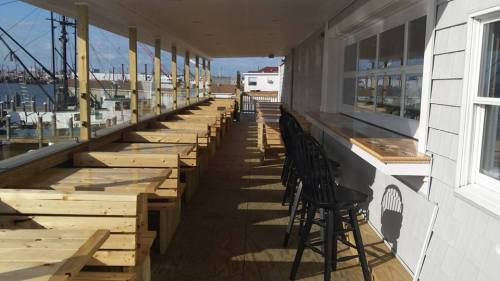 A spacious outdoor dining area with wooden tables and chairs, overlooking a harbor with boats in the background.