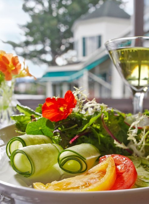 A fresh salad with cucumber rolls, colorful tomatoes, and edible flowers, with a drink in the background.
