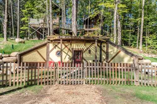 A unique, earthy house with a wooden fence, surrounded by trees and greenery in a forested area.