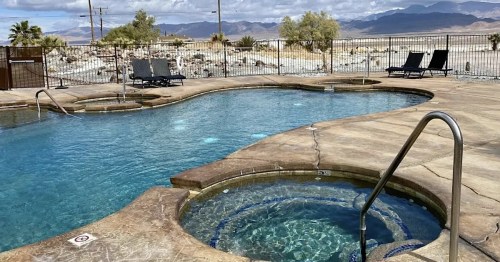 A scenic pool area with a hot tub, surrounded by desert landscape and mountains in the background under a cloudy sky.