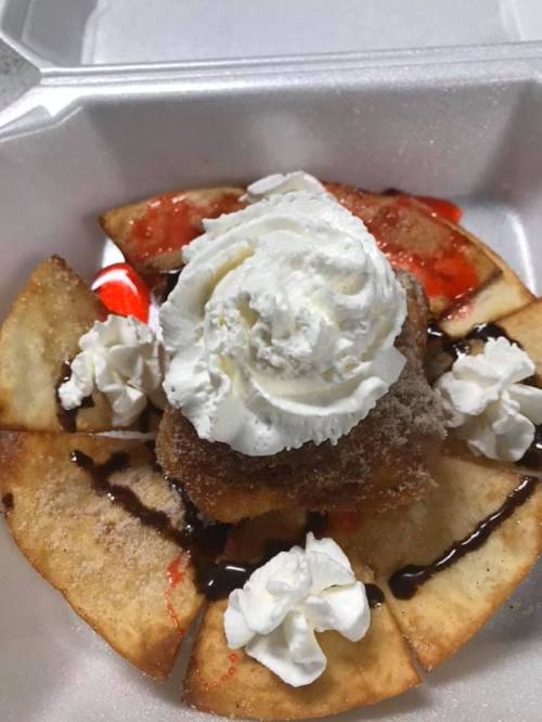 A dessert featuring a fried pastry topped with whipped cream, chocolate drizzle, and strawberry sauce, served on a plate.