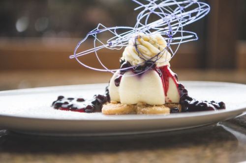 A creamy dessert topped with whipped cream, berry sauce, and decorative sugar strands on a plate.