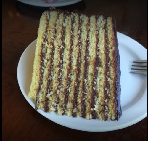 A slice of layered cake with alternating yellow and chocolate layers on a white plate.