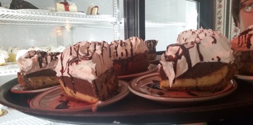 A tray of chocolate cream pies topped with whipped cream and chocolate drizzle, displayed in a bakery case.
