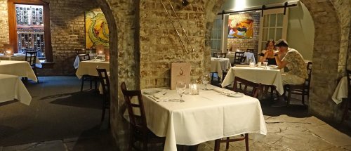 A cozy restaurant with arched brick walls, white tablecloths, and a lone diner at a table. Soft lighting creates a warm atmosphere.
