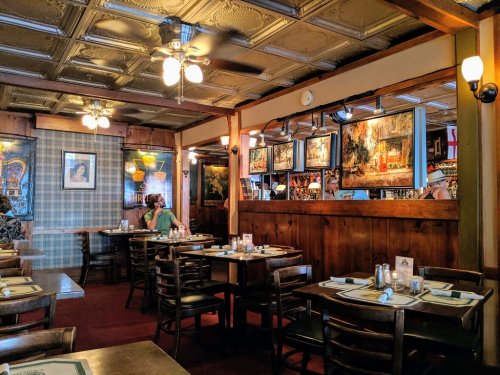 Cozy restaurant interior with wooden walls, tables set for dining, and artwork displayed on the walls.