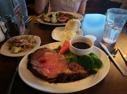A plate of prime rib with broccoli, a side salad, and a glass of water on a table in a restaurant setting.