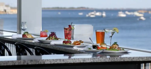A scenic view of a waterfront dining area with various colorful dishes and drinks on a table.