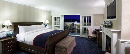 Cozy hotel room with a king bed, fireplace, and balcony access, featuring elegant decor and soft lighting.