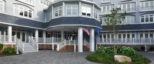 A modern building entrance with a porch, American flag, and landscaped greenery in front.